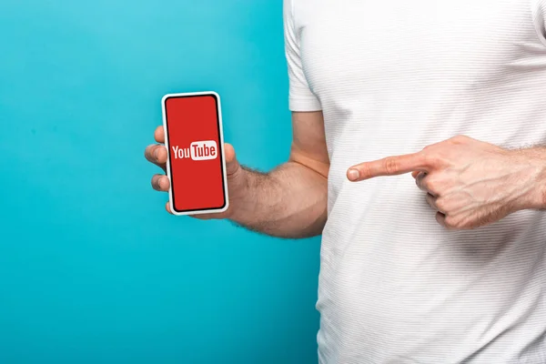 KYIV, UKRAINE - MAY 16, 2019: cropped view of man pointing at smartphone with youtube app, isolated on blue — Stock Photo