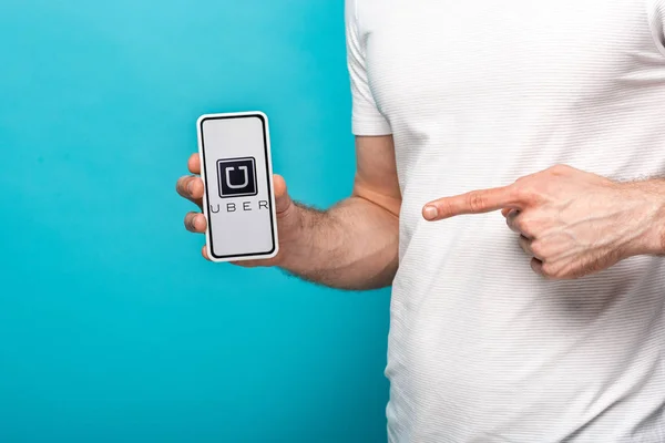 KYIV, UKRAINE - MAY 16, 2019: cropped view of man pointing at smartphone with uber app, isolated on blue — Stock Photo