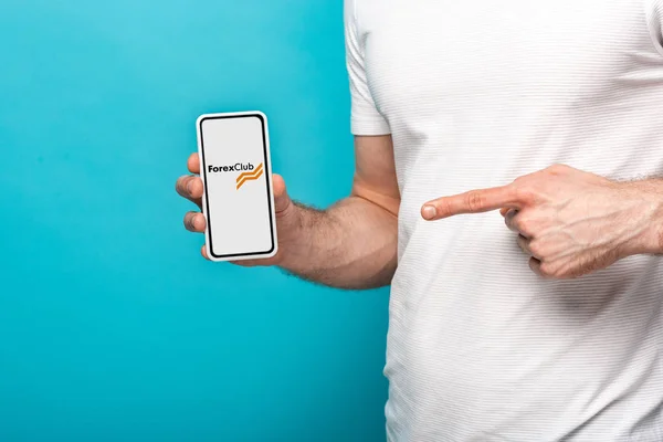 KYIV, UKRAINE - MAY 16, 2019: cropped view of man pointing at smartphone with forex club app, isolated on blue — Stock Photo