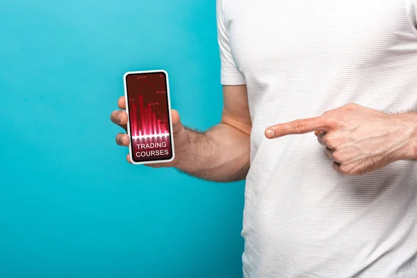 Vue recadrée de l'homme pointant vers smartphone avec cours de trading app, isolé sur bleu — Photo de stock