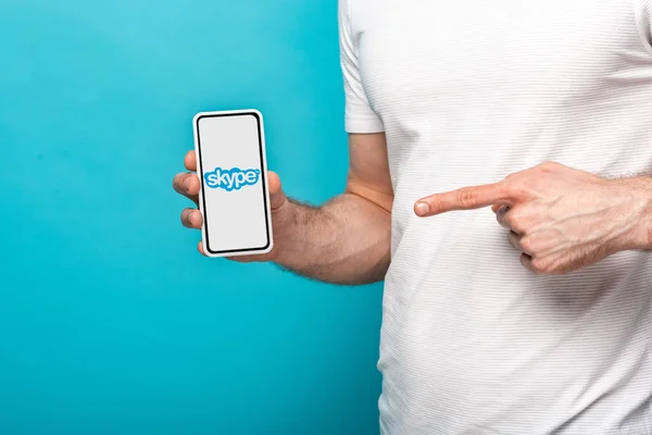 KYIV, UKRAINE - MAY 16, 2019: cropped view of man pointing at smartphone with skype app, isolated on blue — Stock Photo