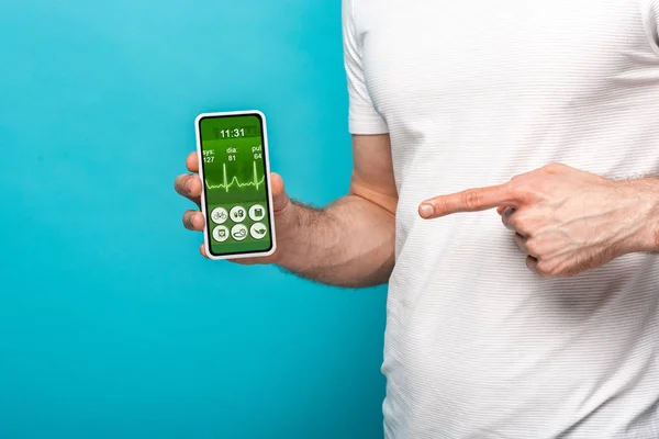 Cropped view of man pointing at smartphone with health app, isolated on blue — Stock Photo