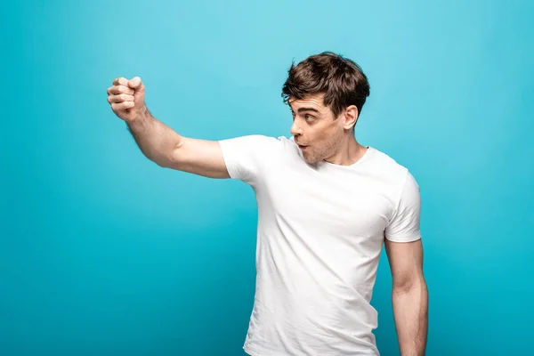 Angry young man looking away and showing fist on blue background — Stock Photo