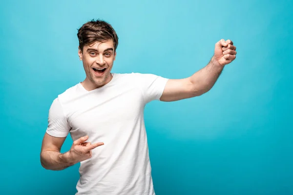 Cheerful young man looking at camera and pointing with finger on blue background — Stock Photo