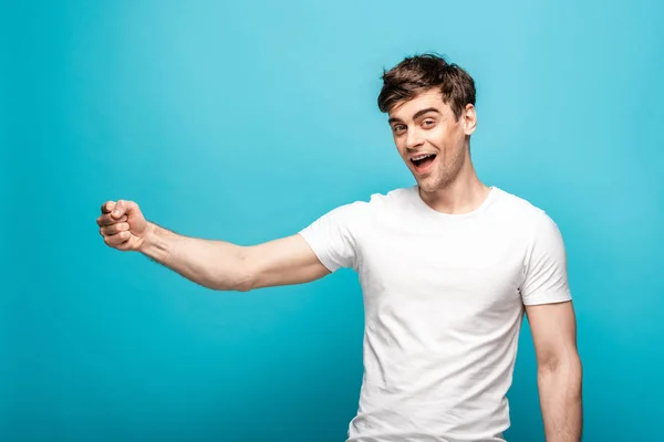 Alegre hombre mostrando puño mientras mira la cámara sobre fondo azul - foto de stock