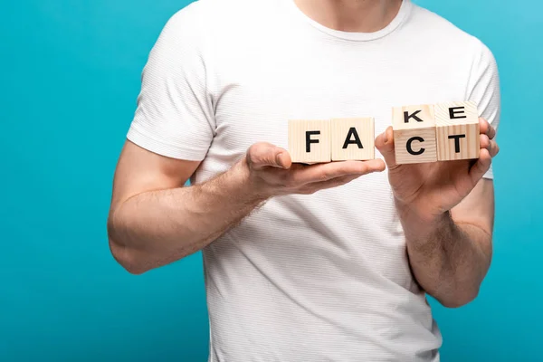 Partial view of man holding wooden cubes with fake fact lettering on blue background — Stock Photo