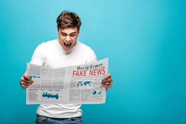 Angry man yelling while reading newspaper with fake news on blue background — Stock Photo