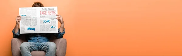 Panoramic shot of man sitting in armchair and reading newspaper with fake news isolated on yellow — Stock Photo