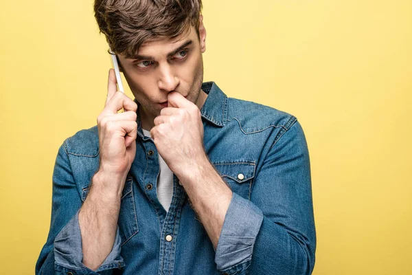 Uomo premuroso distogliendo lo sguardo mentre parla su smartphone isolato sul giallo — Foto stock