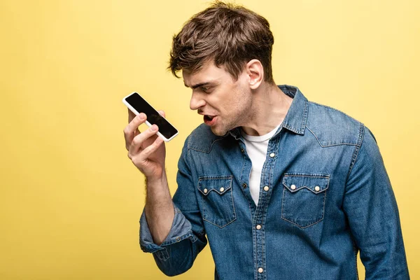 Wütender junger Mann streitet auf Smartphone vor gelbem Hintergrund — Stockfoto