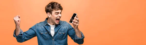 Panoramic shot of angry man quarreling at smartphone and showing fist on yellow background — Stock Photo
