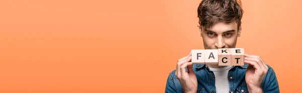Panoramic shot of positive man showing wooden cubes with fake fack lettering isolated on yellow — Stock Photo