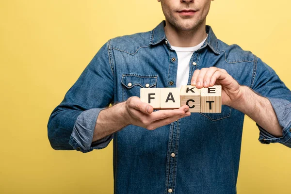 Vista recortada del hombre sosteniendo cubos de madera con letras hecho falso aislado en amarillo — Stock Photo