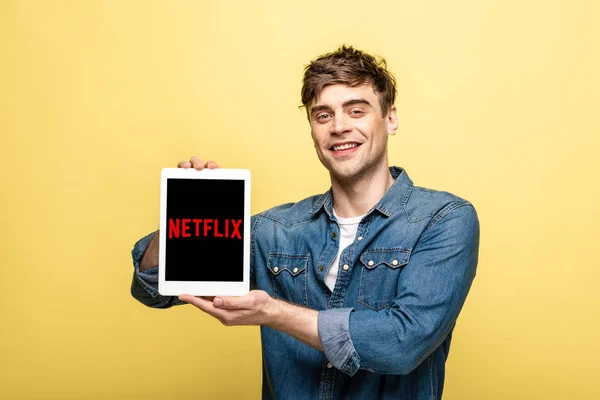 KYIV, UKRAINE - MAY 16, 2019: handsome cheerful man in jeans clothes showing digital tablet with netflix app, isolated on yellow — Stock Photo