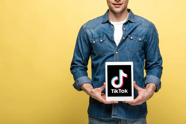 KYIV, UKRAINE - MAY 16, 2019: cropped view of man in jeans clothes showing digital tablet with Tik Tok app, isolated on yellow — Stock Photo