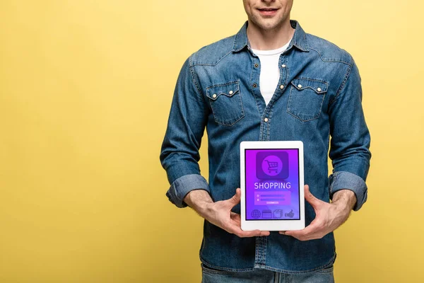 Cropped view of man in denim clothes holding digital tablet with shopping app, isolated on yellow — Stock Photo