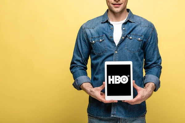 KYIV, UKRAINE - 16 MAI 2019 : vue recadrée de l'homme en jeans vêtements montrant tablette numérique avec application HBO, isolé sur jaune — Photo de stock