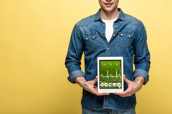 Cropped view of man in denim clothes holding digital tablet with health app, isolated on yellow — Stock Photo