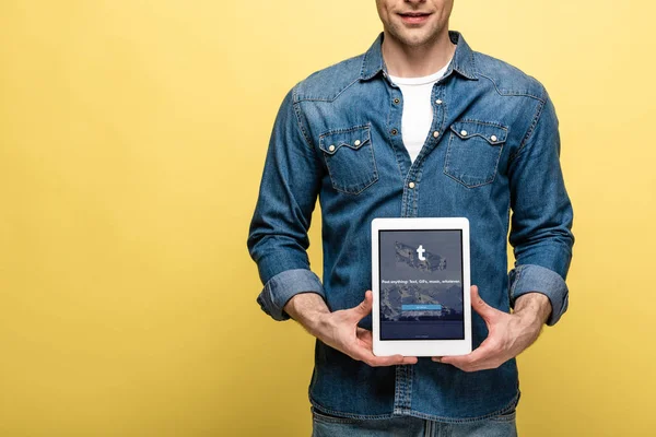 KYIV, UCRAINA - 16 MAGGIO 2019: vista ritagliata dell'uomo in jeans che mostra tablet digitale con app tumblr, isolato su giallo — Foto stock