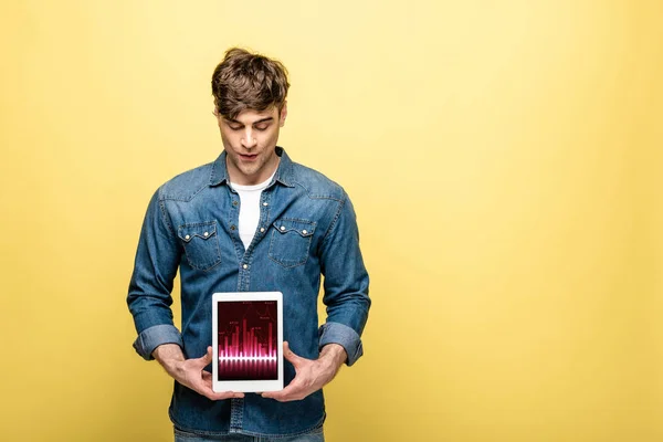 Handsome man in denim clothes looking at digital tablet with graph, isolated on yellow — Stock Photo