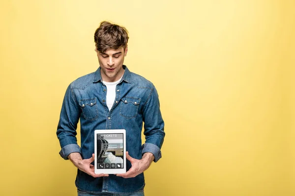Schöner Mann in Jeanskleidung schaut auf digitales Tablet mit Ticket-App, isoliert auf gelb — Stockfoto