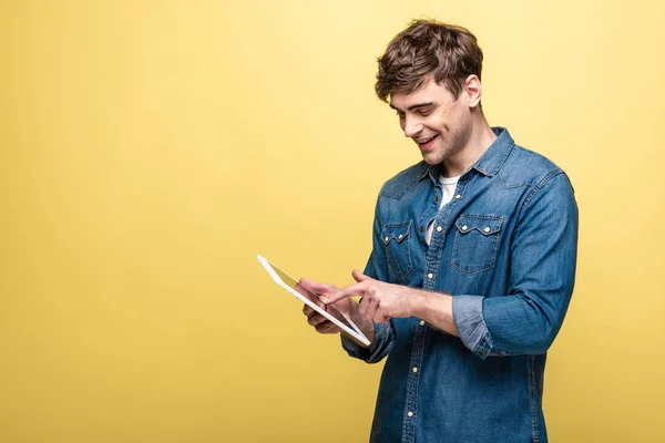 Smiling young man in denim shirt using digital tablet on yellow background — Stock Photo