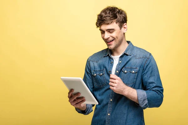 Joven alegre en camisa de mezclilla usando tableta digital sobre fondo amarillo - foto de stock