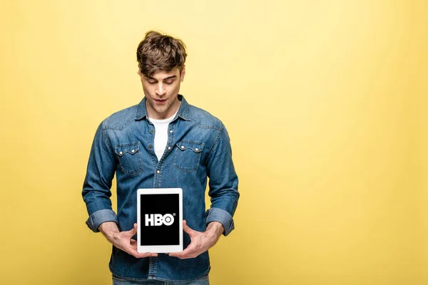 KYIV, UKRAINE - MAIO 16, 2019: homem bonito de jeans olhando para tablet digital com aplicativo HBO, isolado em amarelo — Fotografia de Stock
