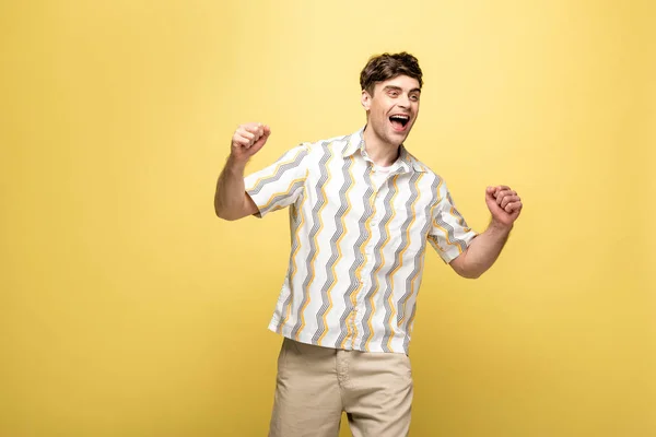 Fröhlicher junger Mann zeigt Siegergeste, während er auf gelbem Hintergrund wegschaut — Stockfoto