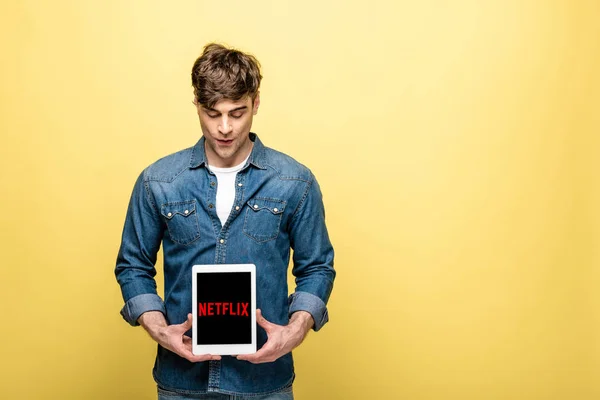 Київ, Україна-16 травня 2019: красивий чоловік в джинсах одяг дивлячись на цифровий планшет з додатком Netflix, ізольований на жовтому — Stock Photo