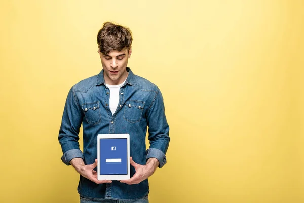 KYIV, UCRAINA - 16 MAGGIO 2019: bell'uomo in jeans che guarda tablet digitale con app facebook, isolato su giallo — Foto stock