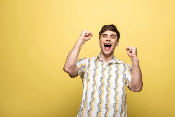 Fröhlicher junger Mann blickt auf und zeigt Siegergeste auf gelbem Hintergrund — Stockfoto