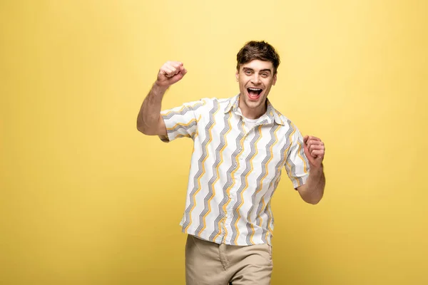 Happy man showing winner gesture while smiling at camera on yellow background — Stock Photo