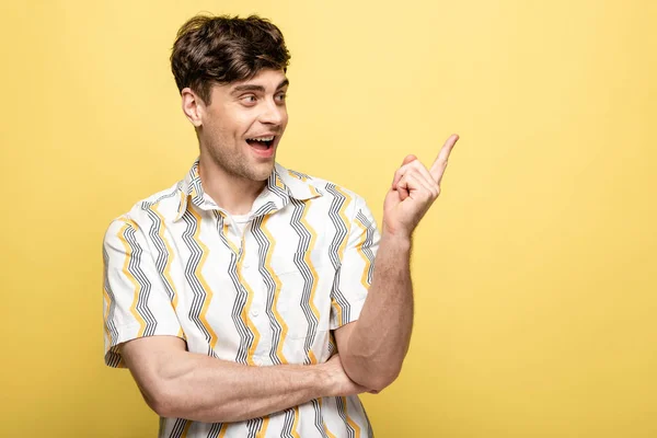 Alegre joven mirando con el dedo mientras mira hacia otro lado sobre fondo amarillo - foto de stock