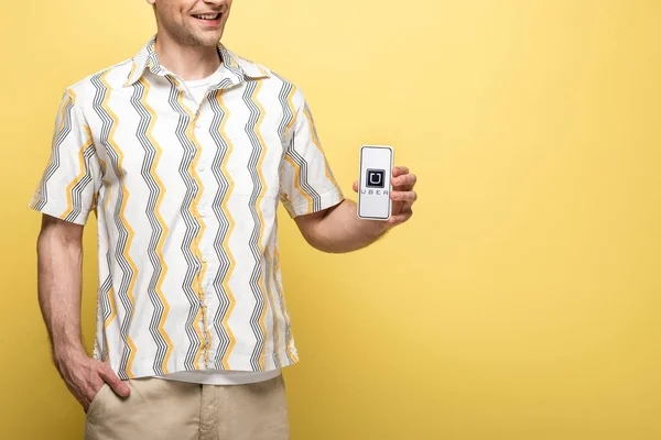 KYIV, UKRAINE - MAY 16, 2019: cropped view of smiling man showing smartphone with uber app, isolated on yellow — Stock Photo