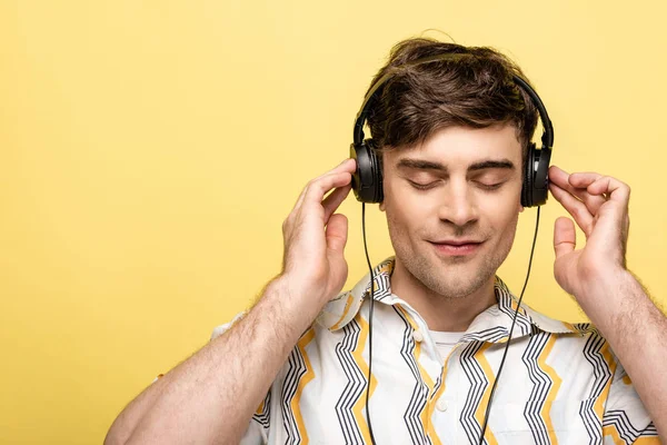 Jeune homme rêveur écoutant de la musique dans des écouteurs avec les yeux fermés sur fond jaune — Photo de stock