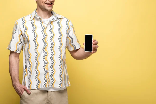 Cropped view of young man holding smartphone with blank screen on yellow background — Stock Photo