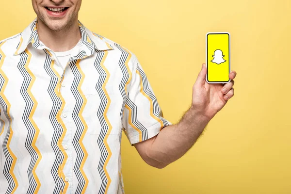 KYIV, UKRAINE - MAIO 16, 2019: visão recortada de homem sorridente mostrando smartphone com aplicativo Snapchat, isolado em amarelo — Fotografia de Stock
