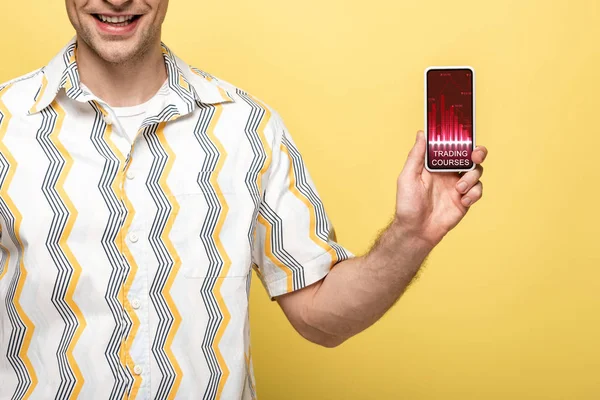 Cropped view of smiling man showing smartphone with trading courses app, isolated on yellow — Stock Photo