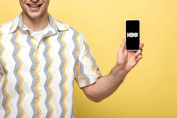 KYIV, UKRAINE - MAIO 16, 2019: visão recortada de homem sorridente mostrando smartphone com aplicativo HBO, isolado em amarelo — Fotografia de Stock