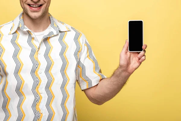 Обрезанный вид улыбающегося мужчины, держащего смартфон с пустым экраном на желтом фоне — стоковое фото