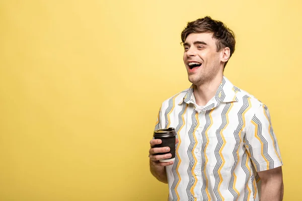 Щасливий чоловік дивиться геть, тримаючи одноразову чашку на жовтому фоні — стокове фото
