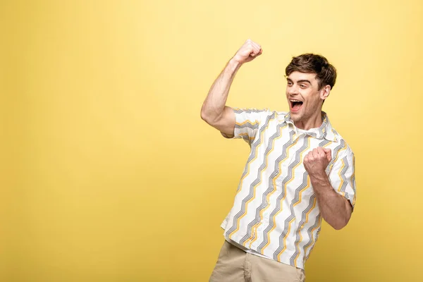 Heureux jeune homme montrant geste gagnant tout en regardant loin sur fond jaune — Photo de stock