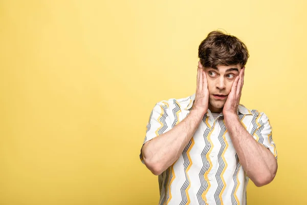 Scoraggiato giovane uomo guardando lontano e tenendo la mano vicino al viso su sfondo giallo — Foto stock