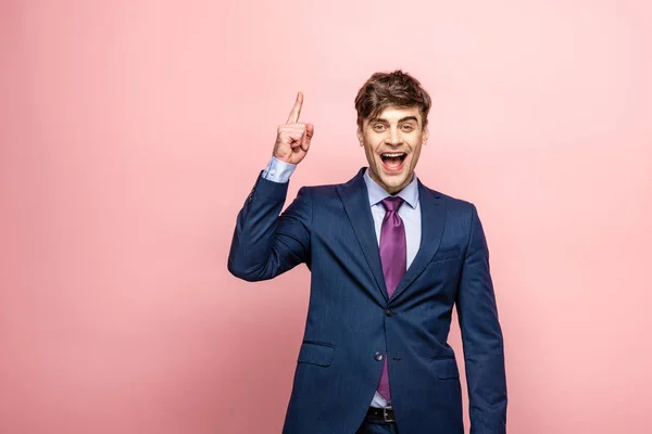 Feliz hombre de negocios mostrando signo de idea y mirando a la cámara en el fondo rosa - foto de stock