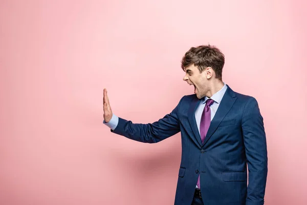 Раздраженный бизнесмен показывает стоп-жест, глядя в сторону на розовый фон — стоковое фото