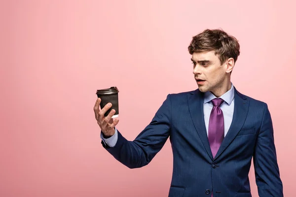 Sorprendido hombre de negocios mirando taza desechable sobre fondo rosa - foto de stock