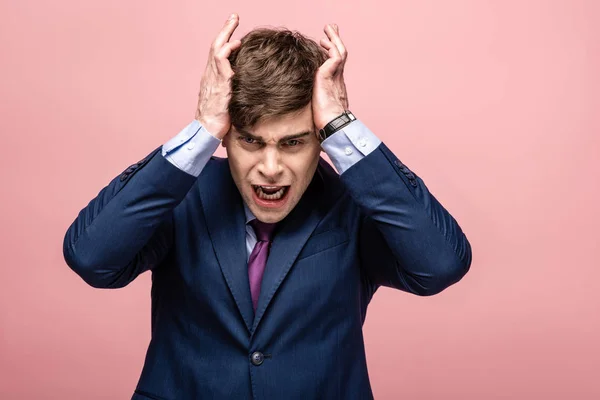 Unhappy businessman holding hands near head while looking at camera isolated on pink — Stock Photo