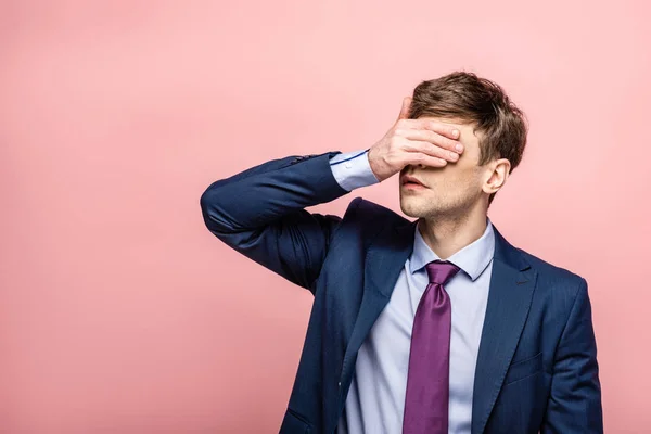 Upset businessman covering eyes with hand on pink background — Stock Photo