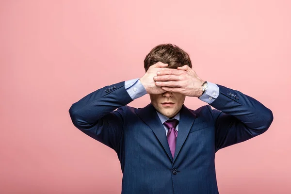 Homem de negócios jovem em terno cobrindo olhos com mãos isoladas em rosa — Fotografia de Stock